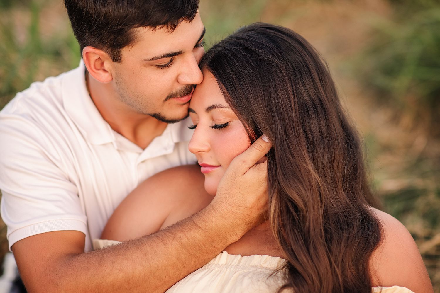 Romantic couple embracing outdoors at golden hour, man tenderly holding woman's face in a warm natural setting.
