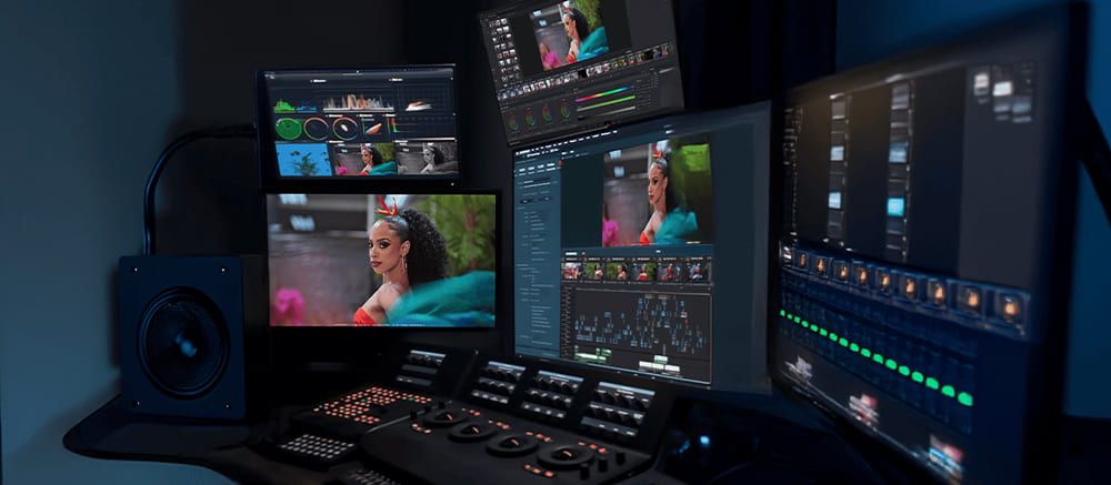 Professional video editing workspace with multiple monitors showing media files and editing software in a dark room.