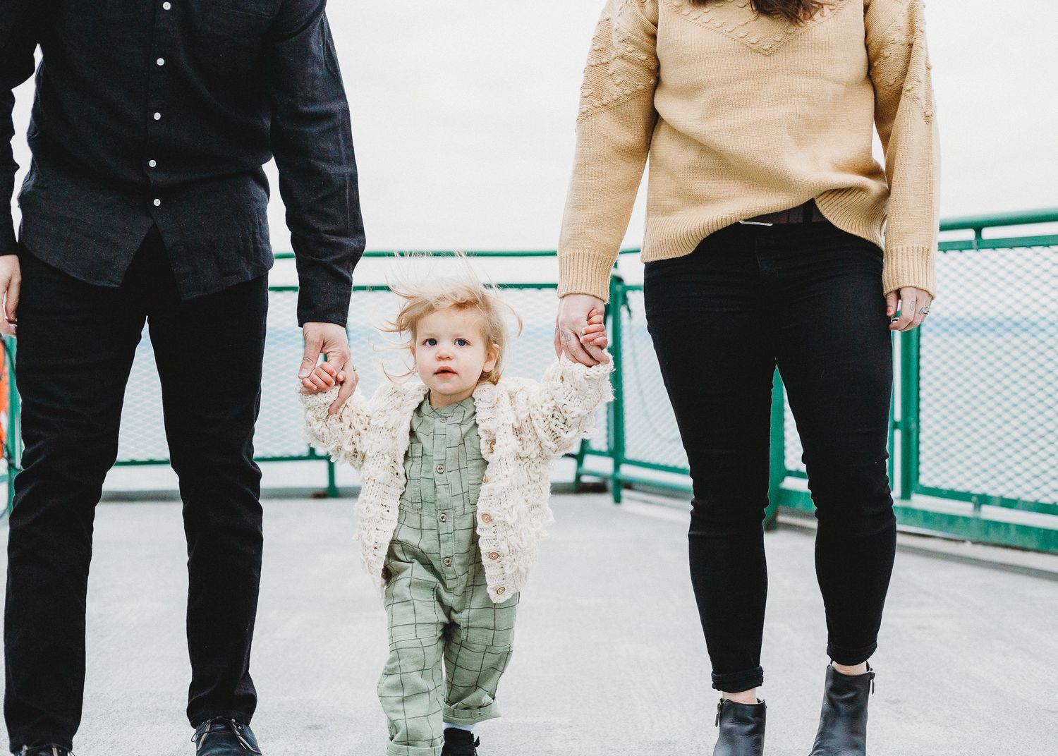 Small child walks while holding hands with adults on what appears to be a ferry deck.