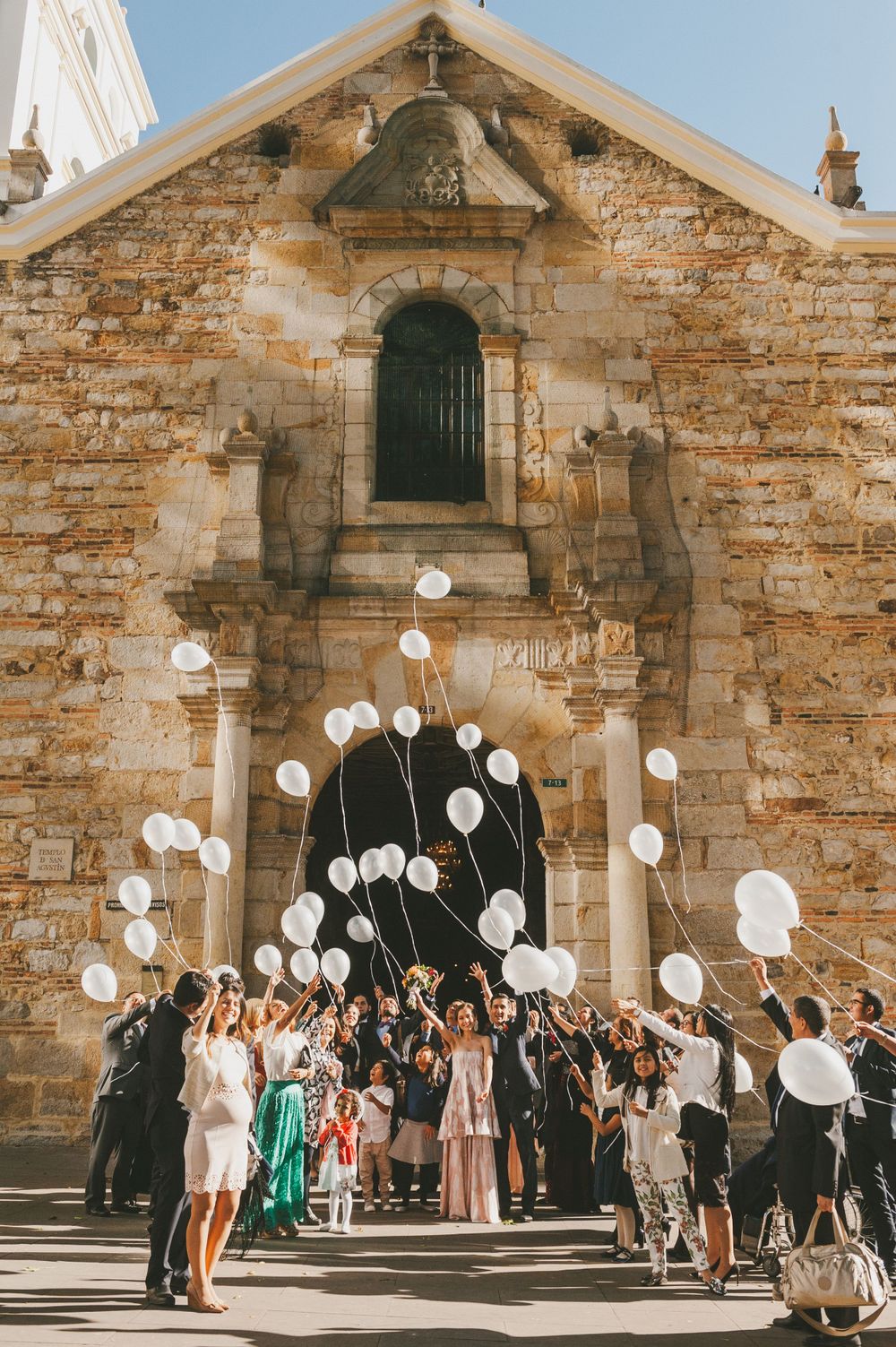 Wedding guests cheering the newlyweds with white baloons.