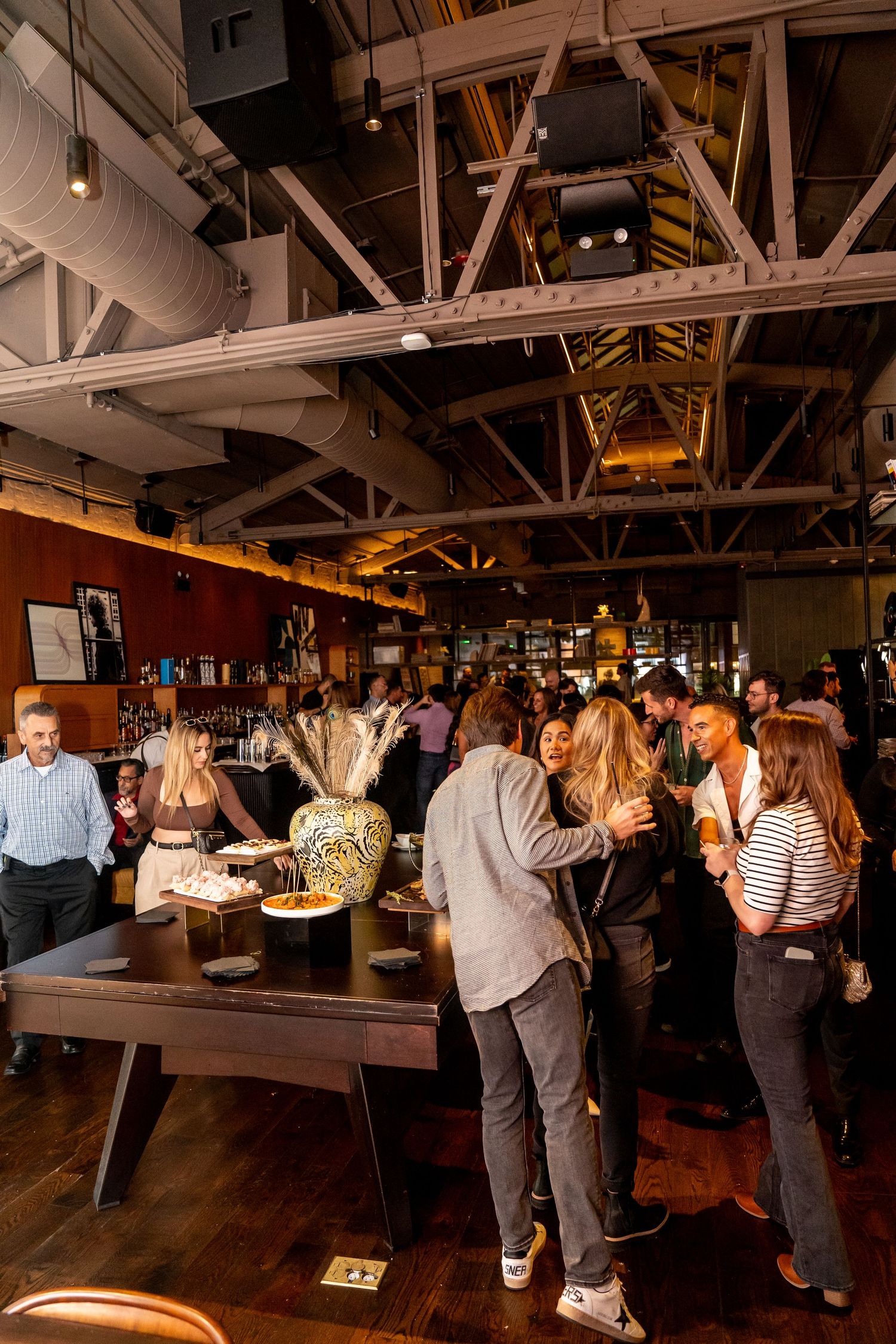 Crowded bar interior with exposed wooden beams and industrial ceiling showing patrons mingling.