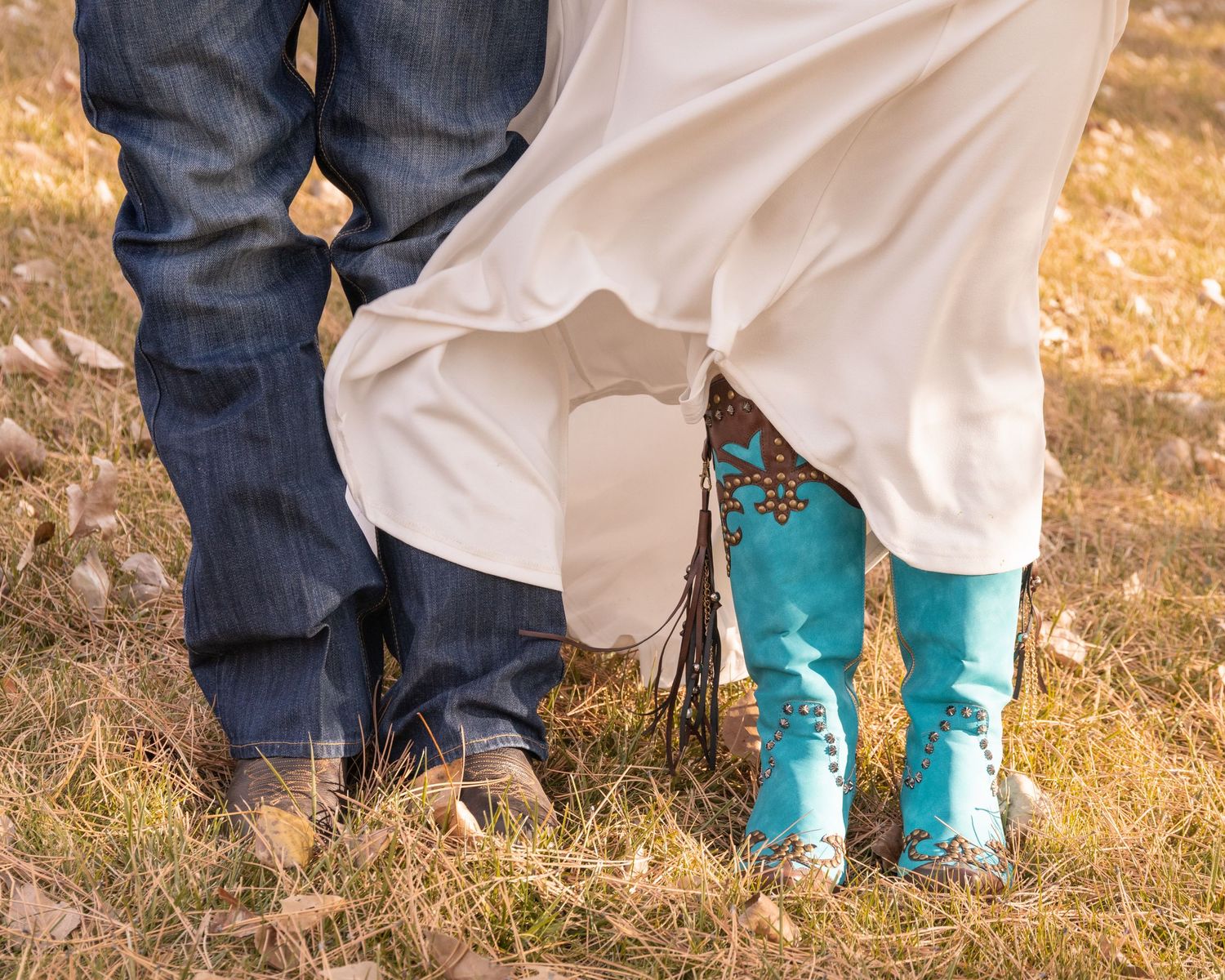 Close-up of denim jeans and turquoise cowboy boots against golden grass background.