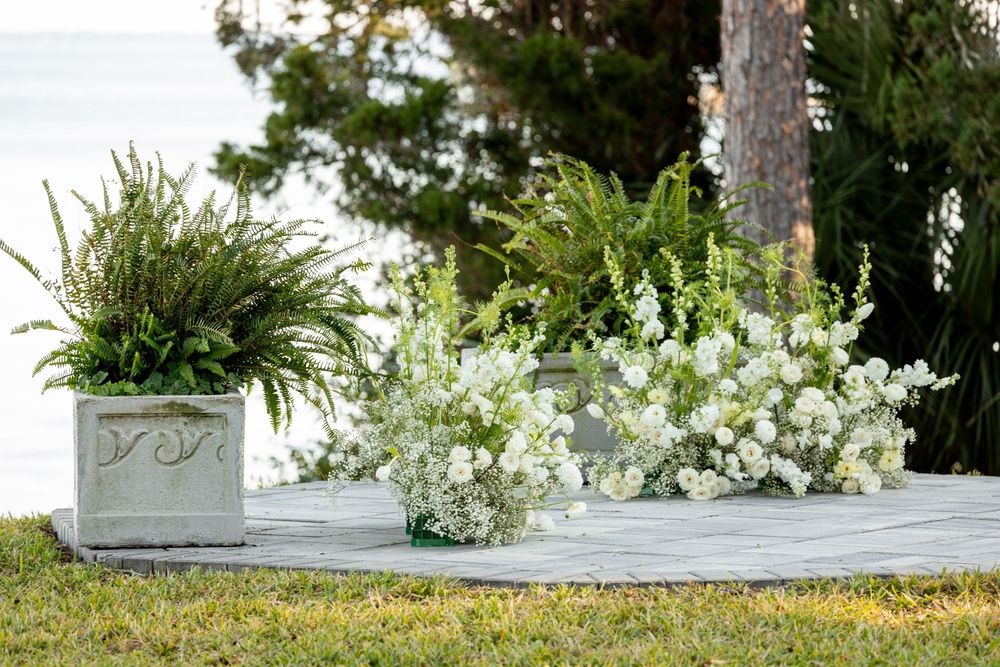 White floral arrangements in gray planters create an elegant outdoor wedding ceremony setup.