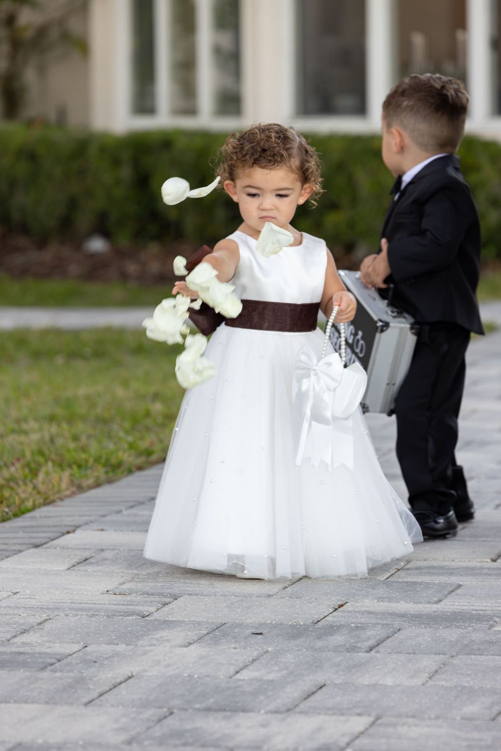 Young attendants in formal wedding attire walking on stone pathway during ceremony.