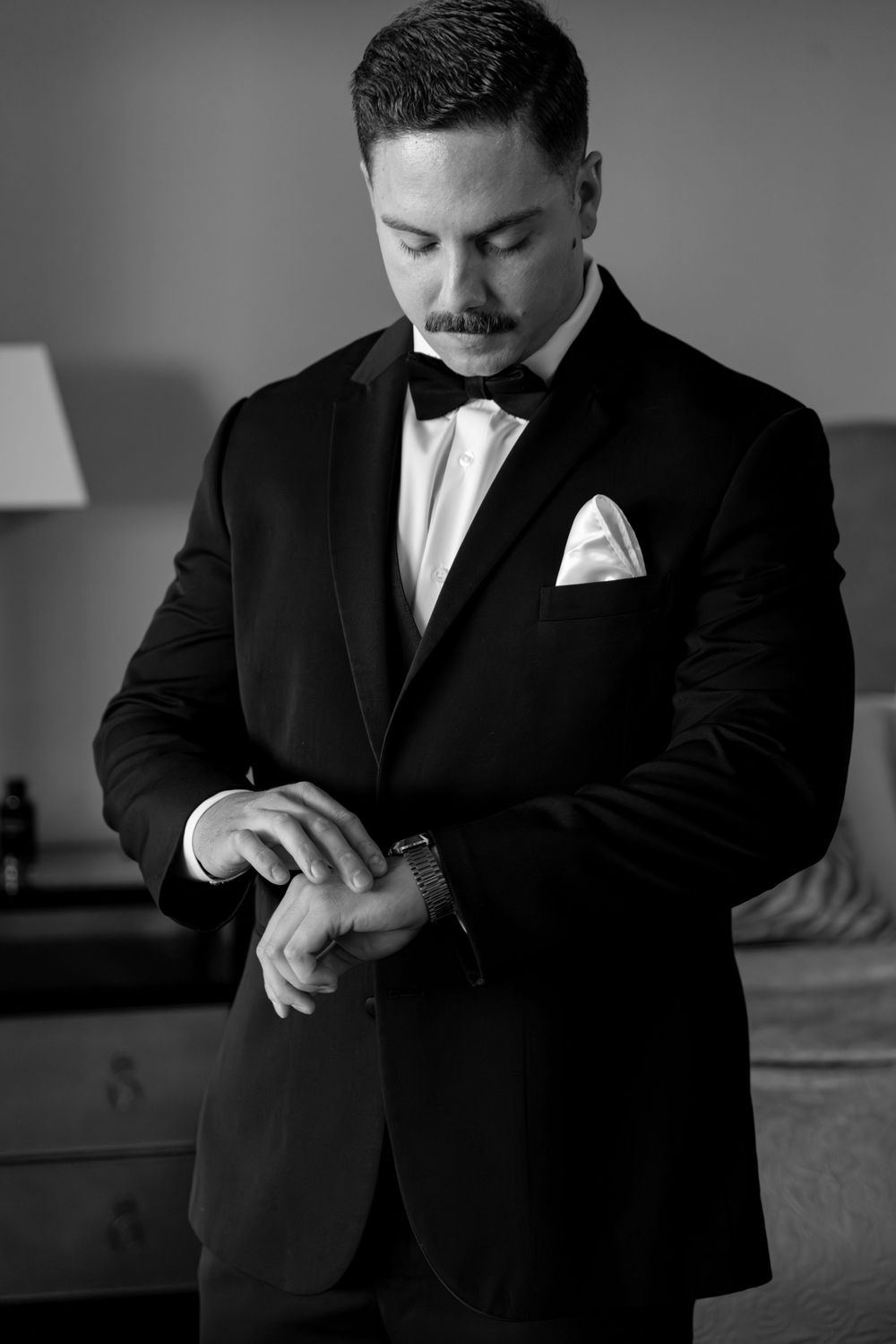 Black and white photos show a groom adjusting his suit and tie before the wedding ceremony.