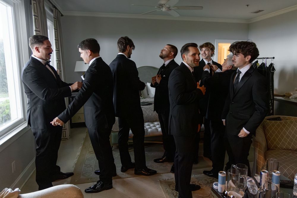A line of people in formal black attire stand in a row against a white wall during what appears to be a ceremony.