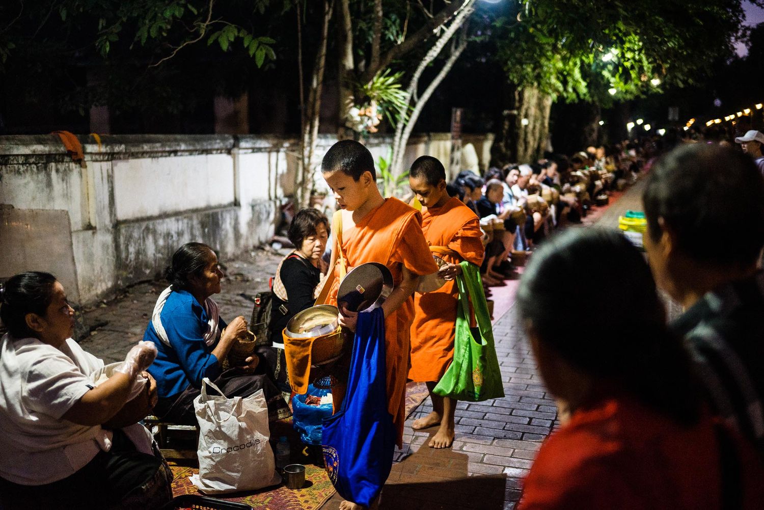 People in orange and blue shirts gather around tables at a community event in a dimly lit space.