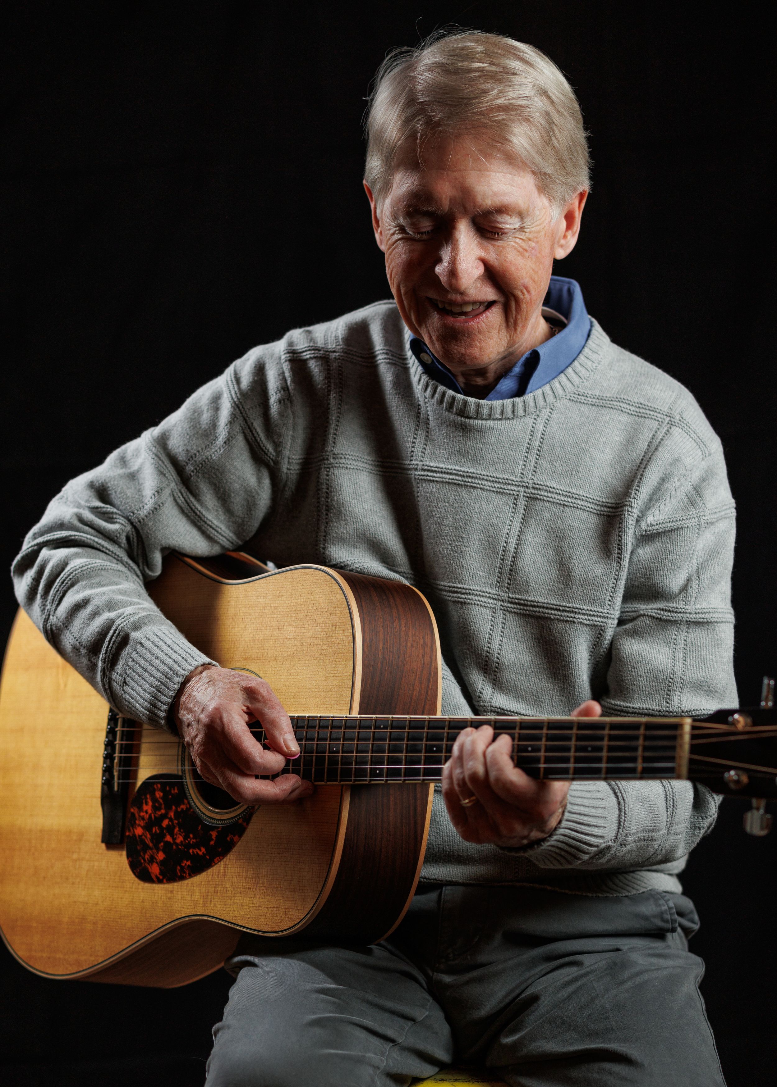 A person in a gray sweater plays an acoustic guitar while sitting down, shown in a series of connected photos.