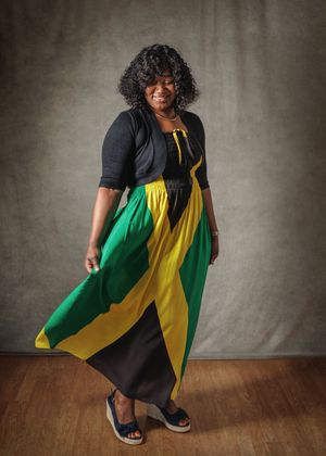 A person wearing a colorful dress in green, yellow and black twirls on a wooden floor against a gray backdrop.