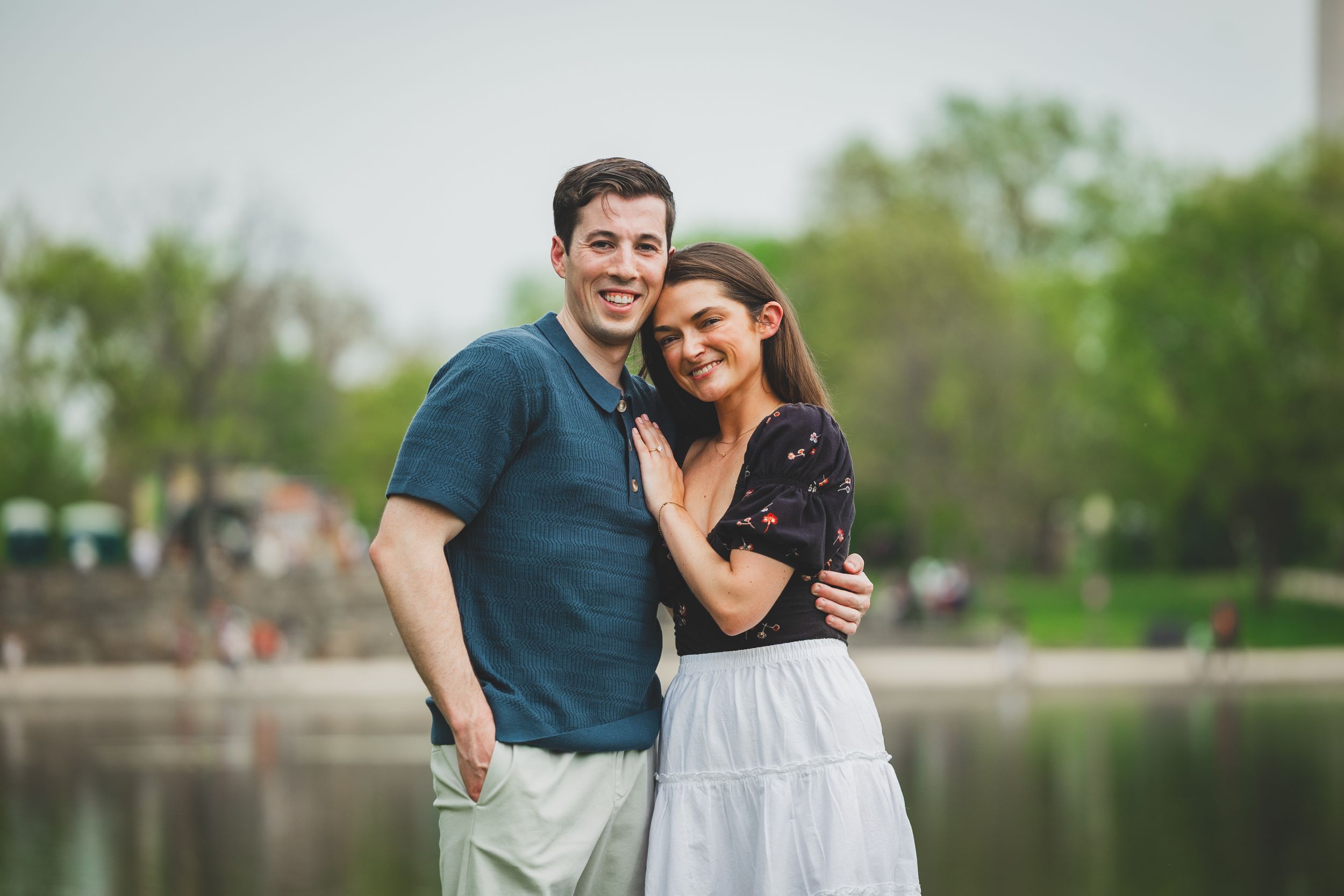 A couple shares an intimate moment while walking together in a park near a lake on a spring day.