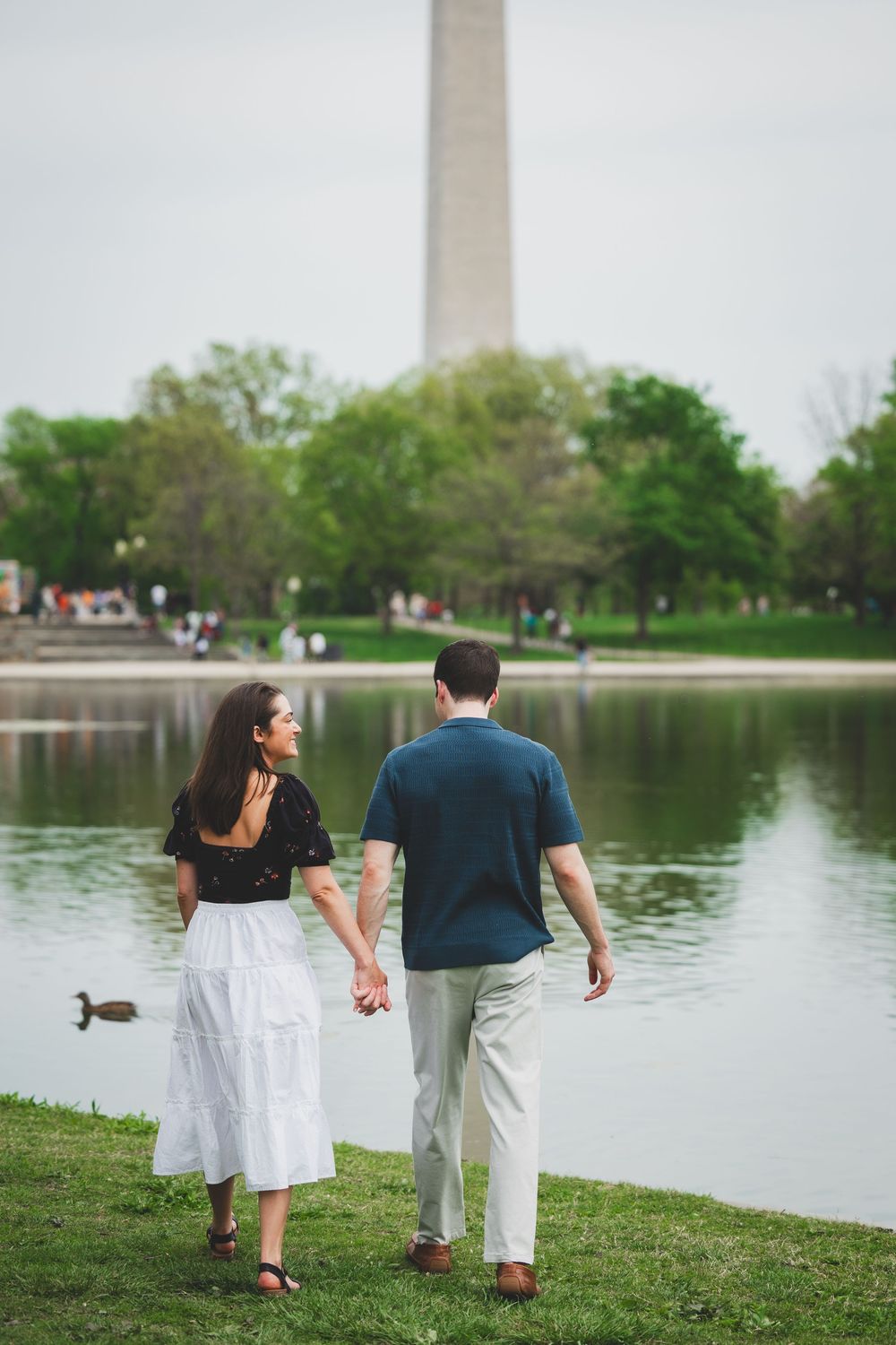 Couple walking along the reflecting pool at the National Mall in Washington DC with the Washington Monument visible.