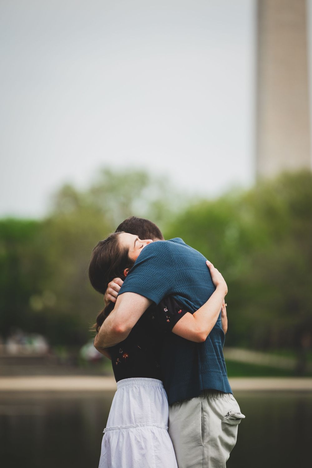 Two people embrace in an emotional hug outdoors against a blurred natural background.