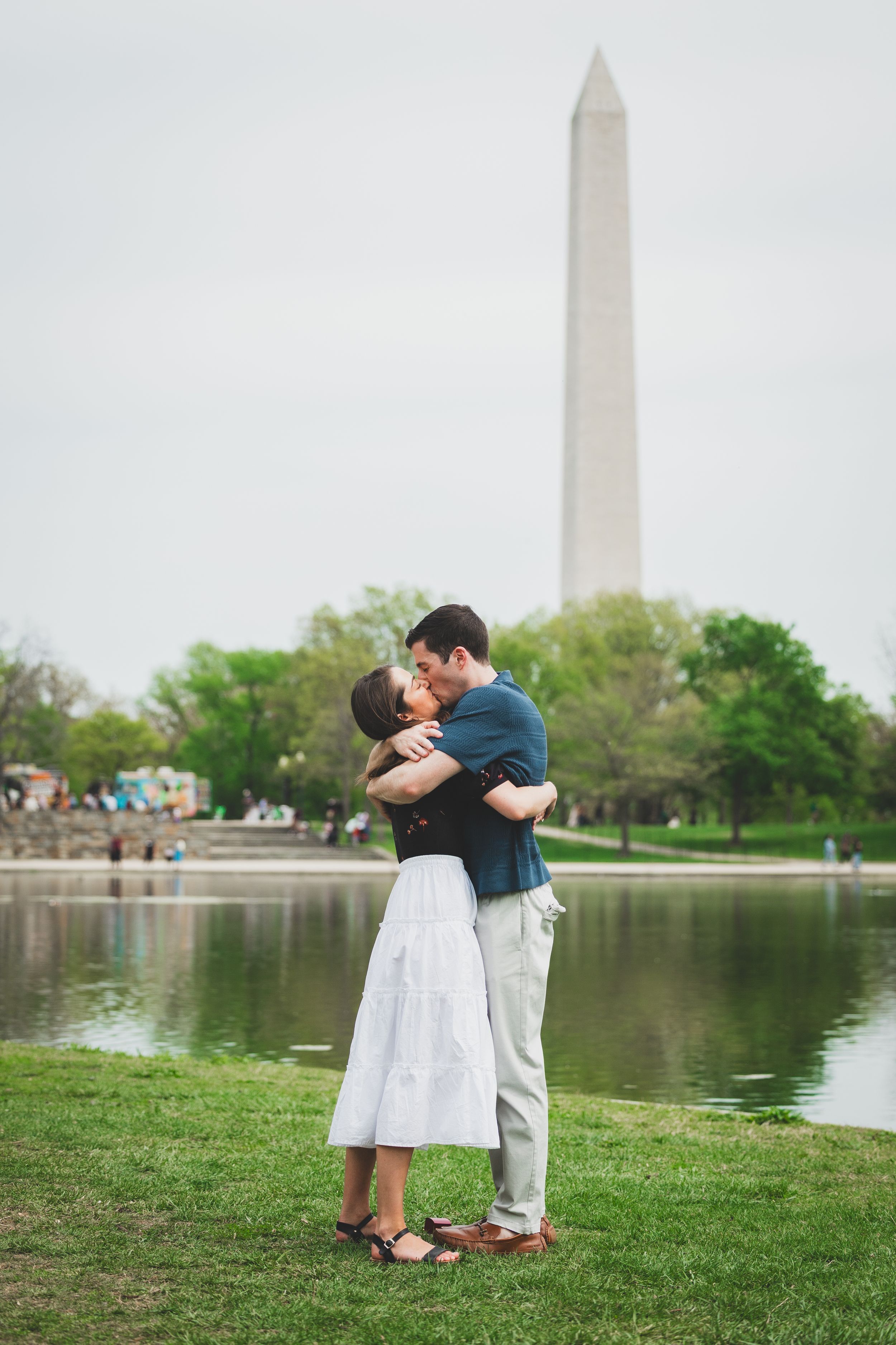 Romantic couple embraces by the Tidal Basin with the Washington Monument rising in the background on a spring day.