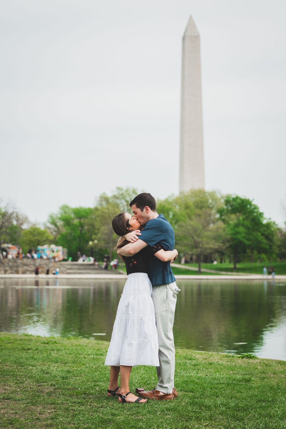 Romantic couple embraces by the Tidal Basin with the Washington Monument rising in the background on a spring day.