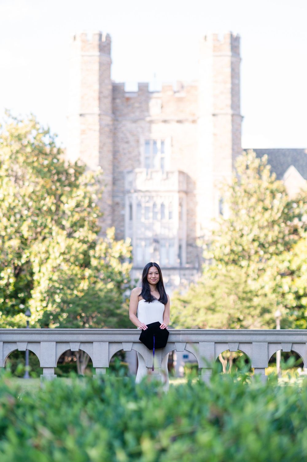 A person sits on a stone wall overlooking lush green grass with historic castle-like architecture in the background.