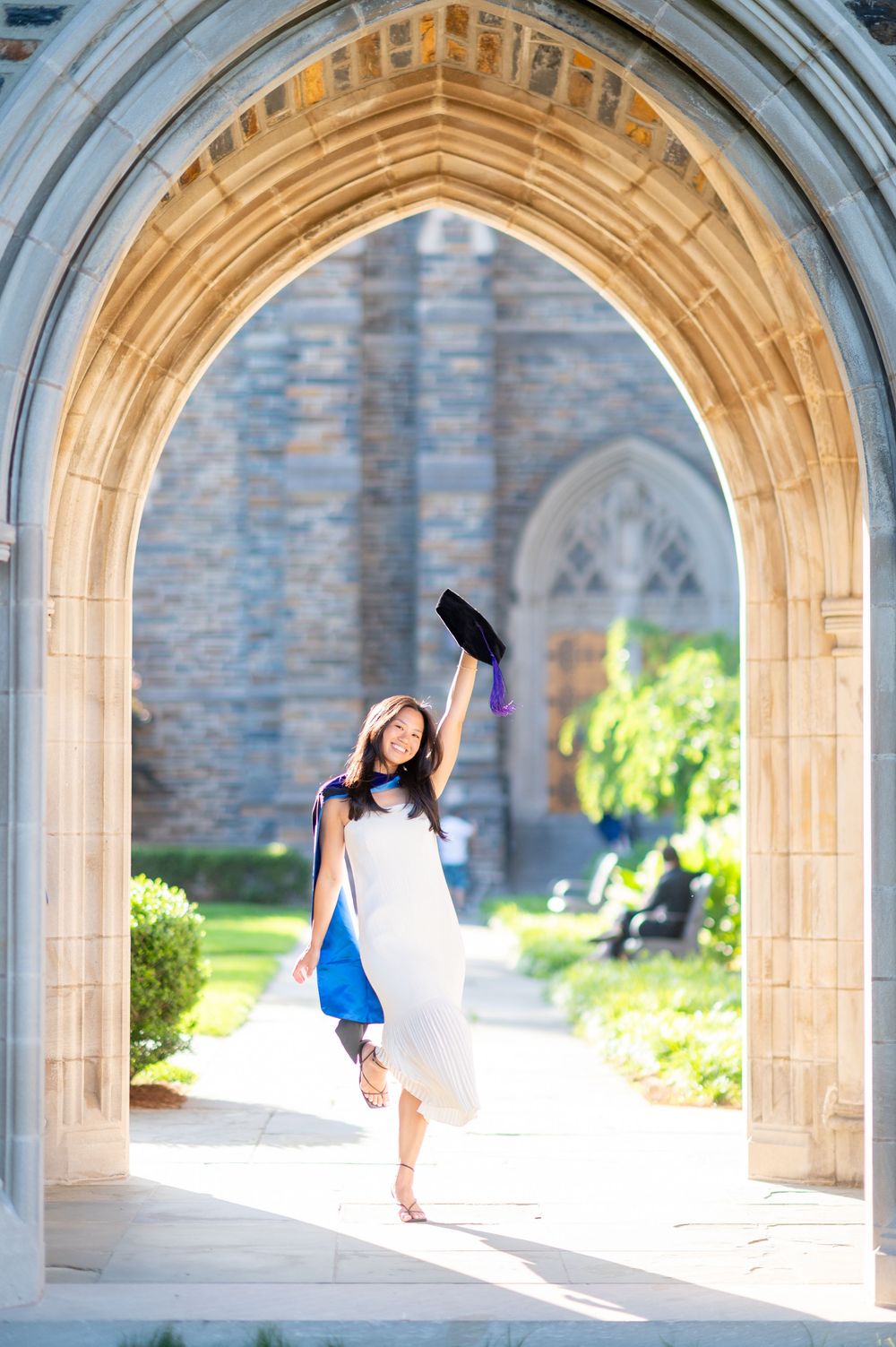 A dancer in a white dress performs graceful movements under stone archways at a historic building.