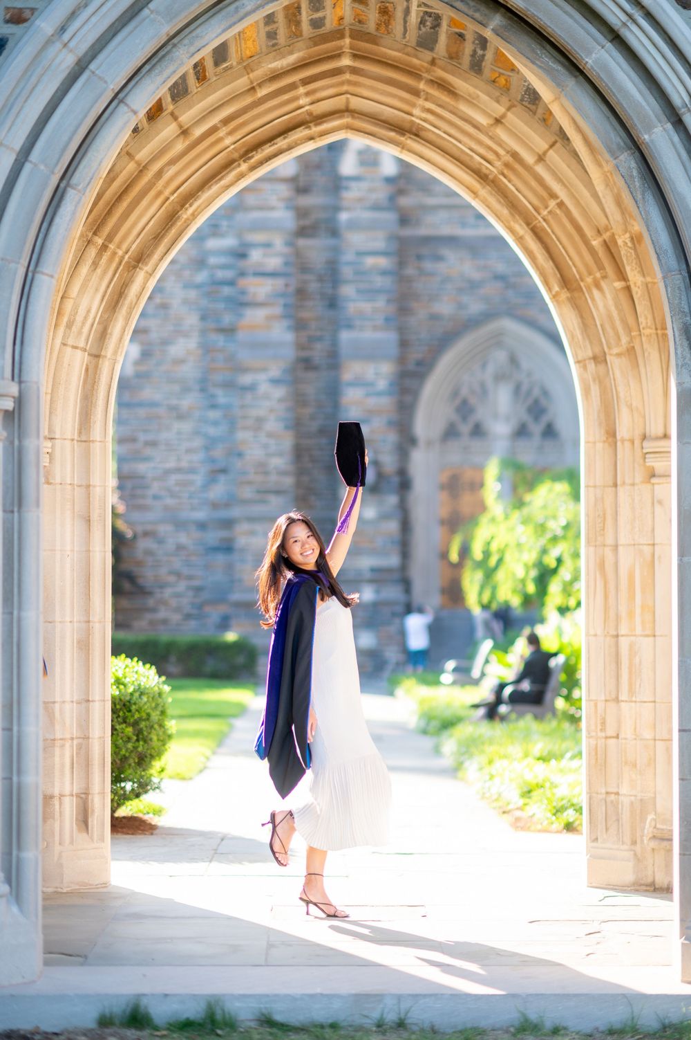 Graduation photos taken in a beautiful stone archway with sunlit columns and greenery in the background.