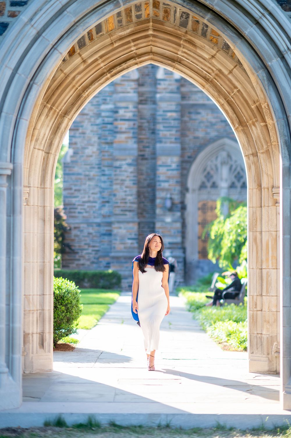 Person walking through a series of Gothic stone archways on a sunny day at a university campus.
