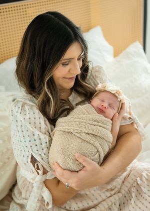 A tender moment captured in soft lighting shows a parent cradling and bonding with a newborn baby wrapped in beige knit.