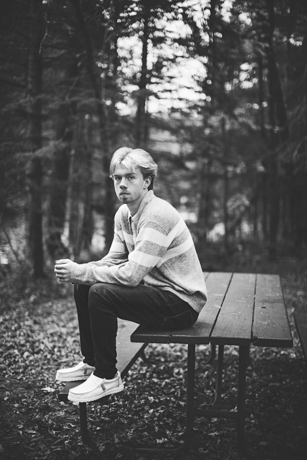 Black and white photo of someone sitting thoughtfully on a wooden bench in a moody forest setting.