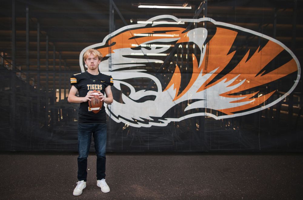 Someone stands in front of a large black wall featuring a stylized orange and white tiger head logo mural.