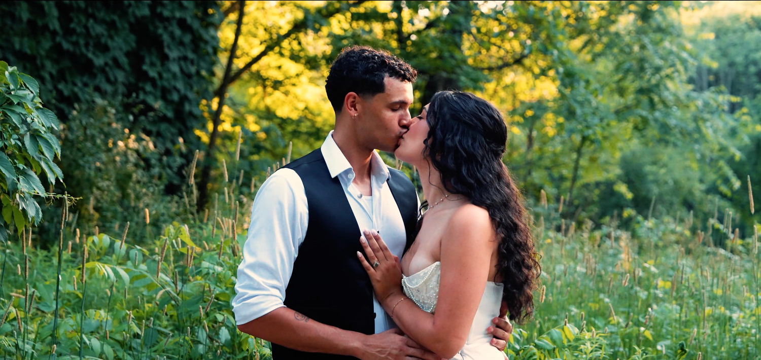 A couple shares an intimate moment in a lush green meadow during golden hour lighting.