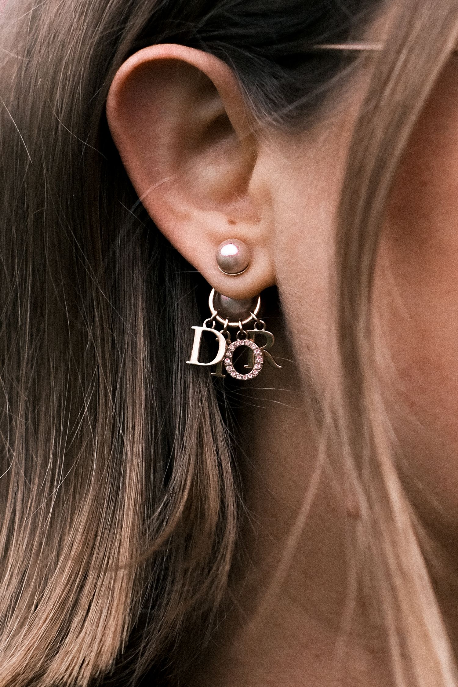 Close-up view of multiple delicate silver and gold earrings displayed on ears against a neutral background.