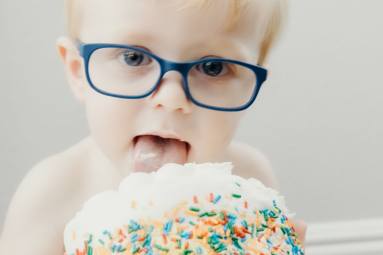Close-up of someone wearing blue glasses enjoying a sprinkle-covered dessert.