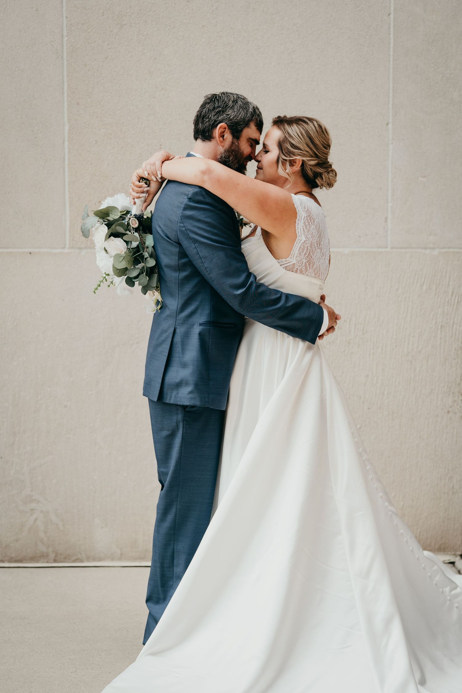 Wedding couple embracing in romantic poses against neutral wall background.