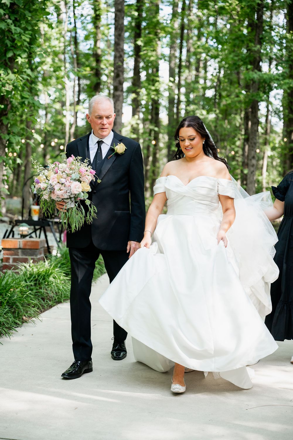 A couple walking together on a paved pathway surrounded by lush greenery.