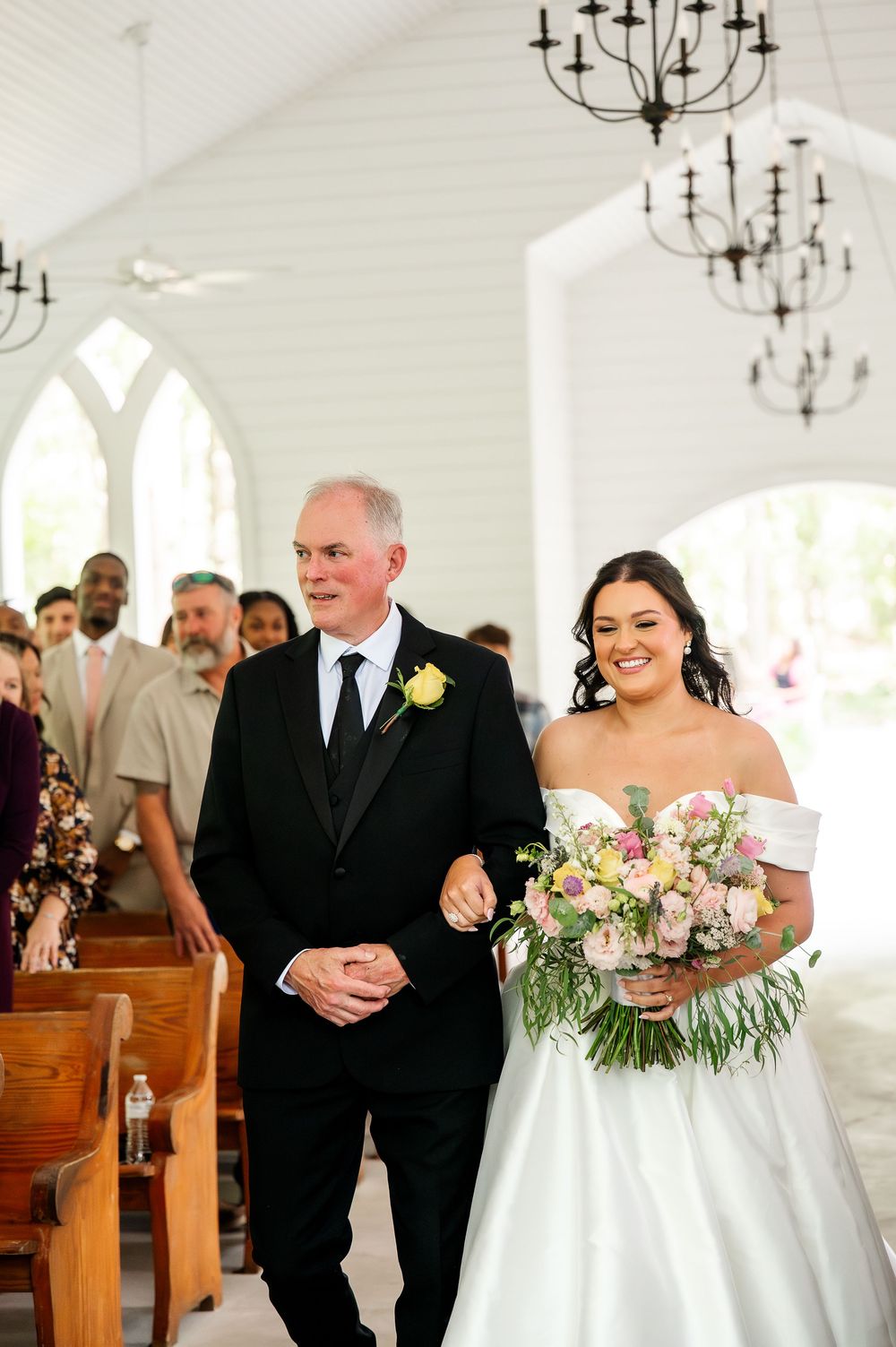 A traditional wedding ceremony taking place inside a white chapel with wooden pews.