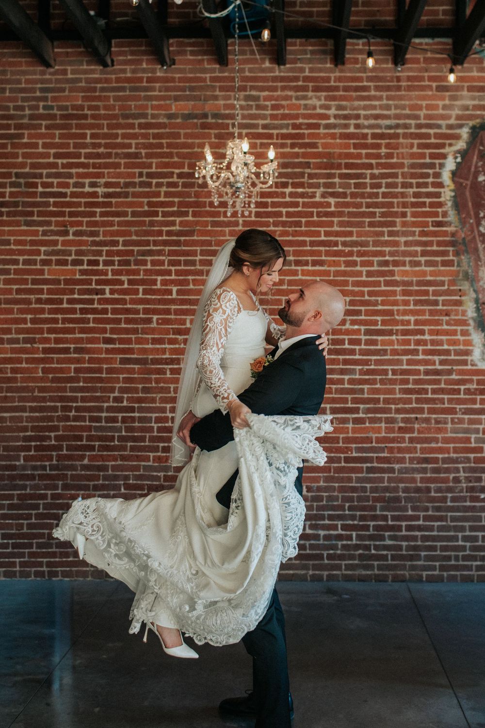 Romantic dip pose showcasing flowing lace wedding dress against industrial brick backdrop.