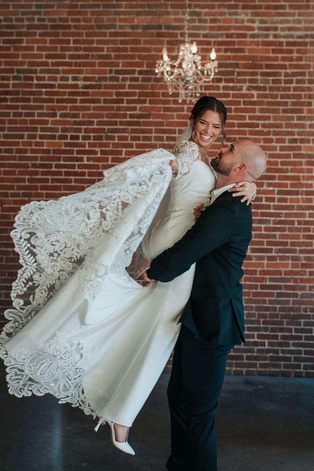 Dramatic wedding dance dip pose with lace dress flowing against rustic brick wall background.