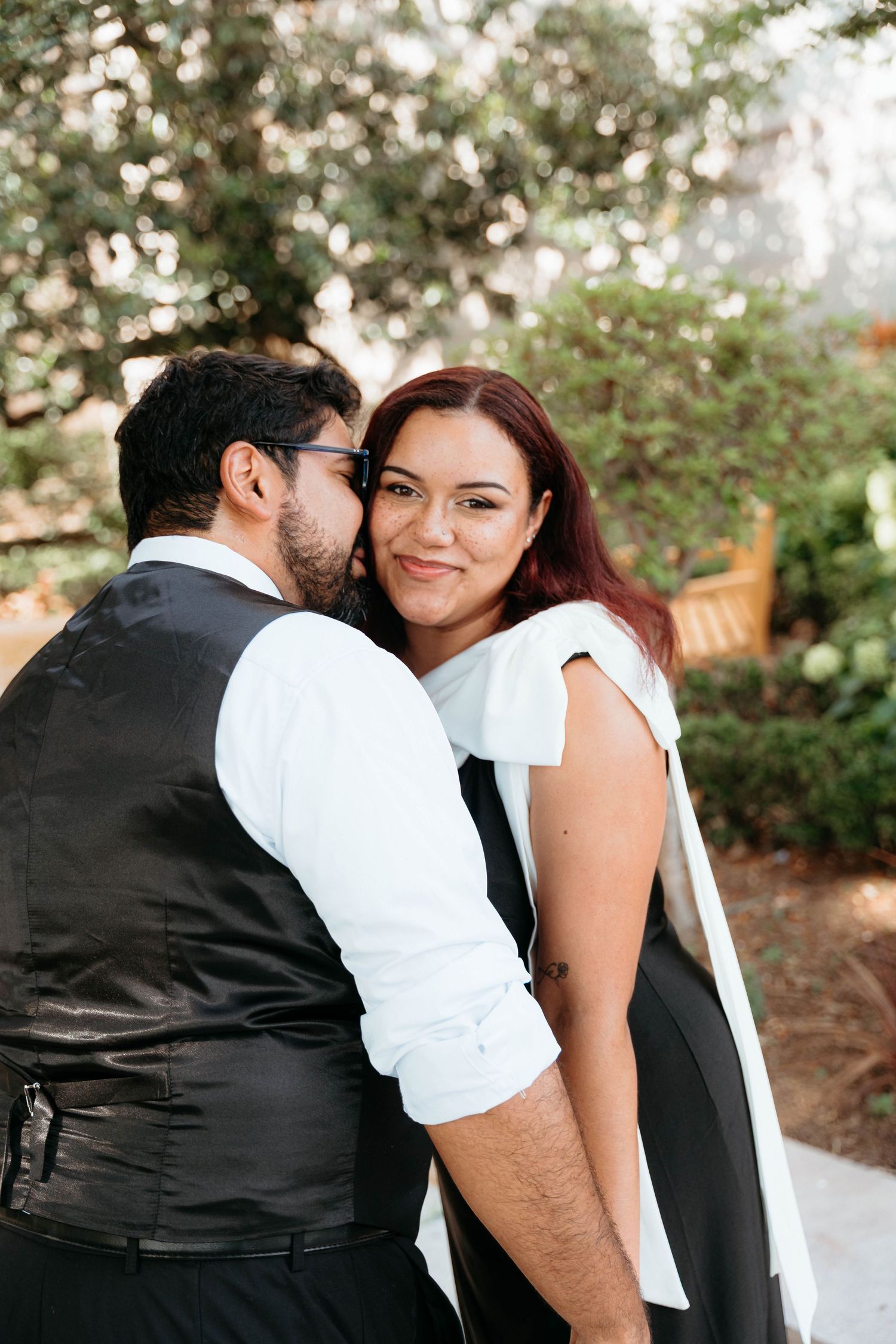 A romantic couple embraces outdoors in formal attire during a photo session in a garden setting.