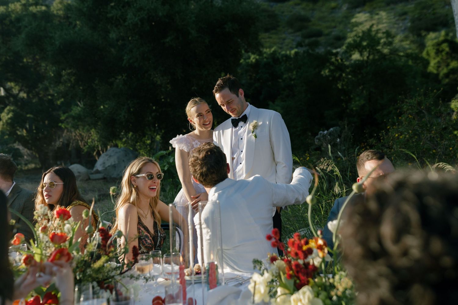 Outdoor garden wedding reception with elegant table settings and colorful floral arrangements during golden hour.