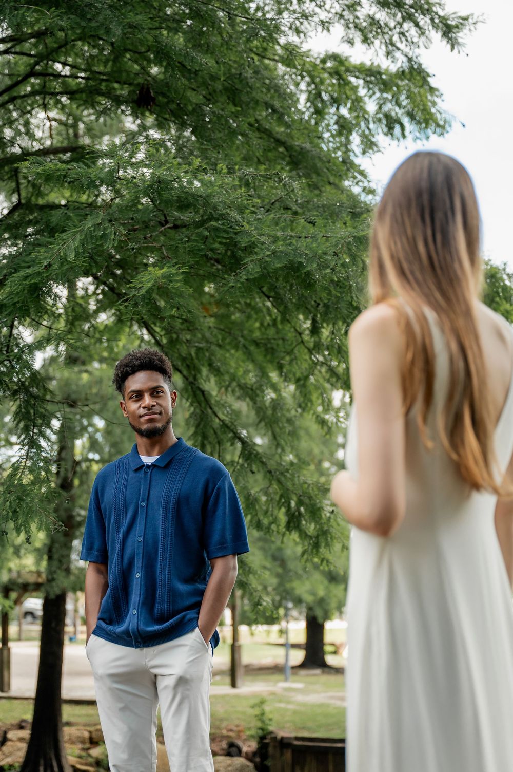 Couple in coordinated white and navy outfits posing among trees in a park.