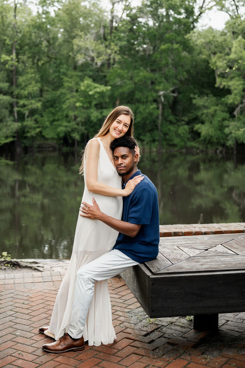 Couple sitting together on a bench by a peaceful lake surrounded by trees.