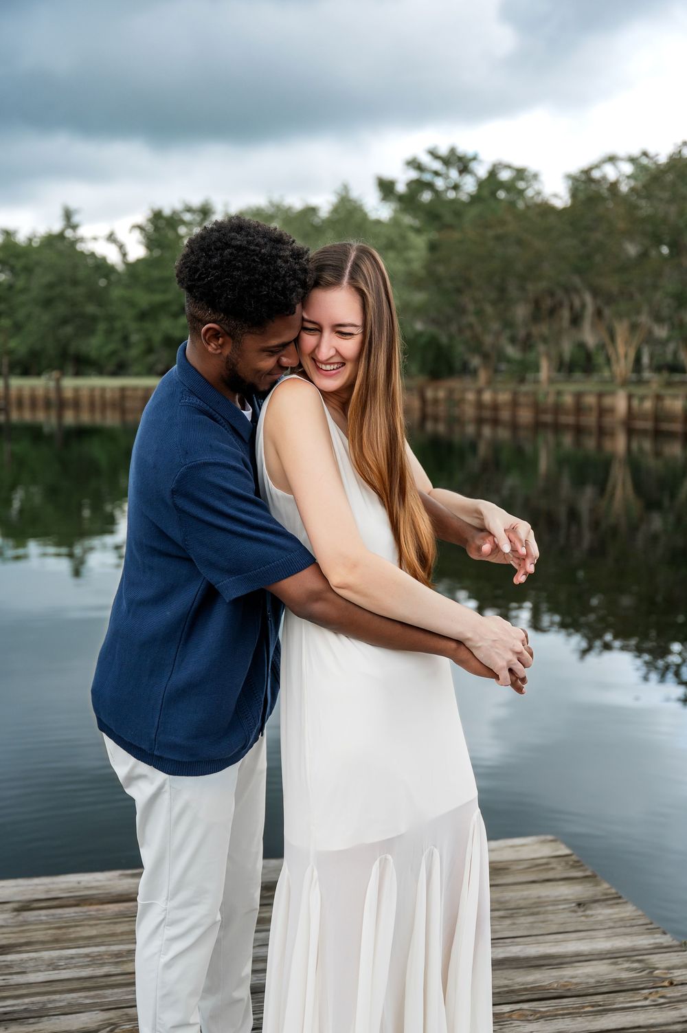Couple shares playful moments on a wooden dock by a serene lake.