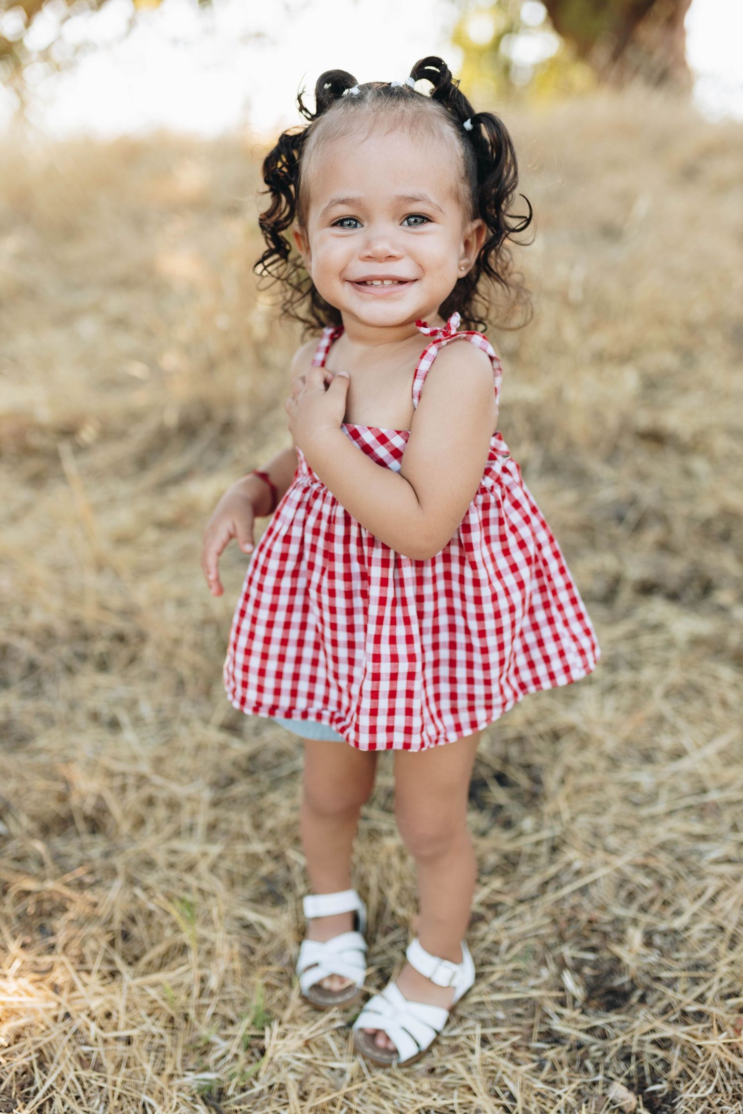 Toddler girl smiling outdoors during a milestone photography session in natural light.