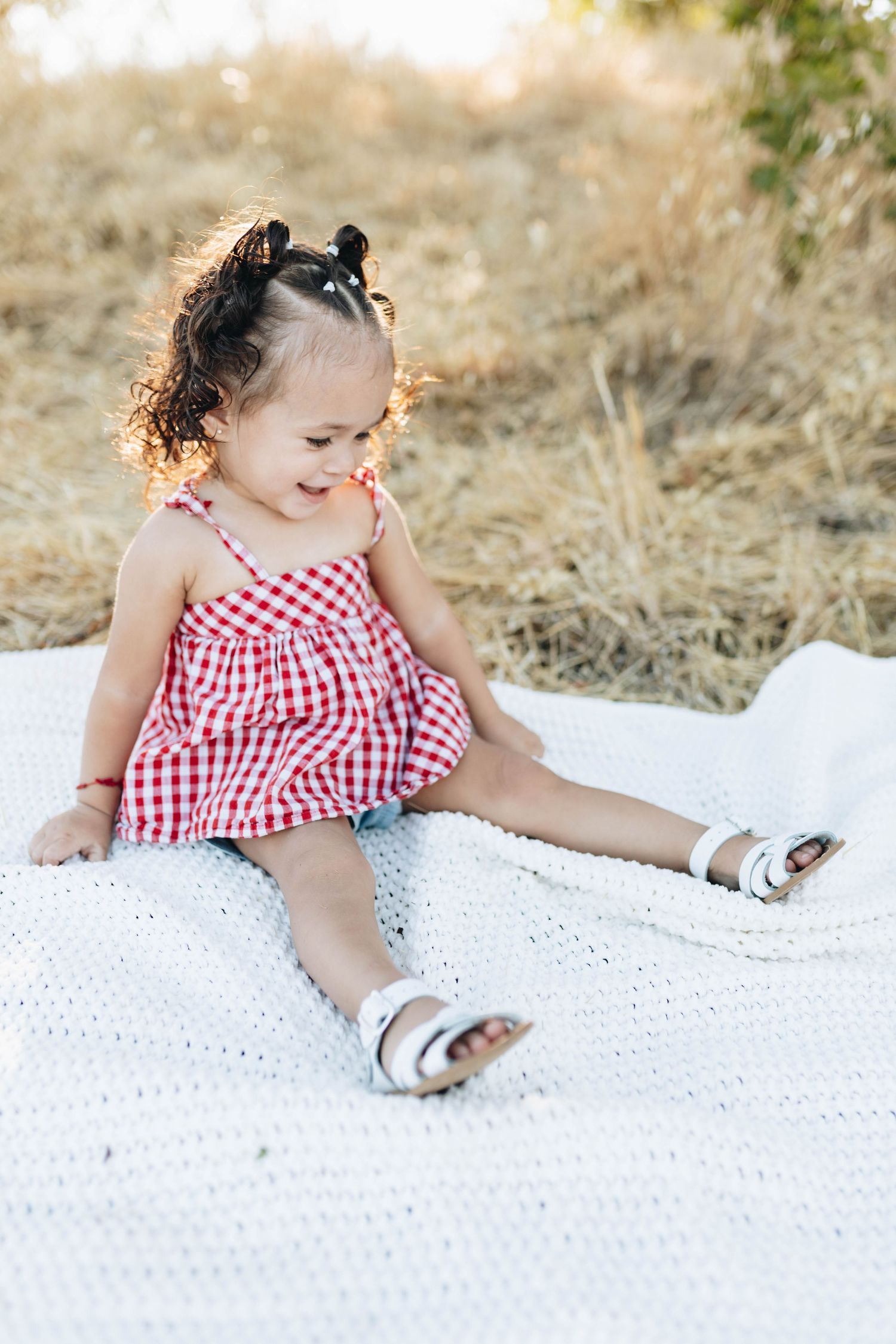 Toddler sitting outdoors during a milestone photography session, smiling in natural light.