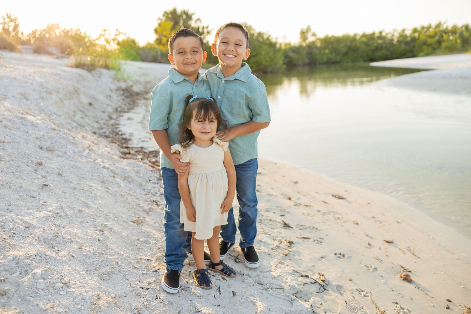 Three children standing together on the beach during a family photography session.