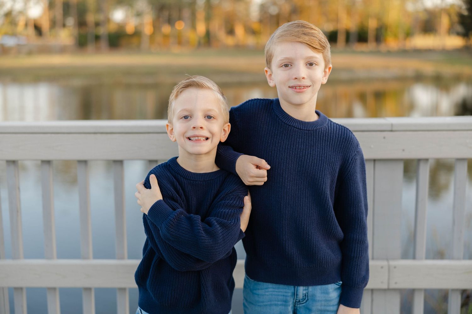 Two young boys standing together and smiling during an outdoor family photography session.