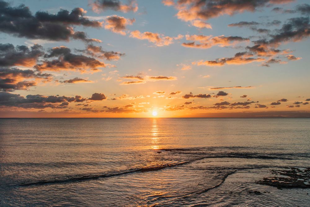 Tramonto arancione vibrante sulle acque in Puglia con nuvole spettacolari che riflettono la luce dorata sulle onde