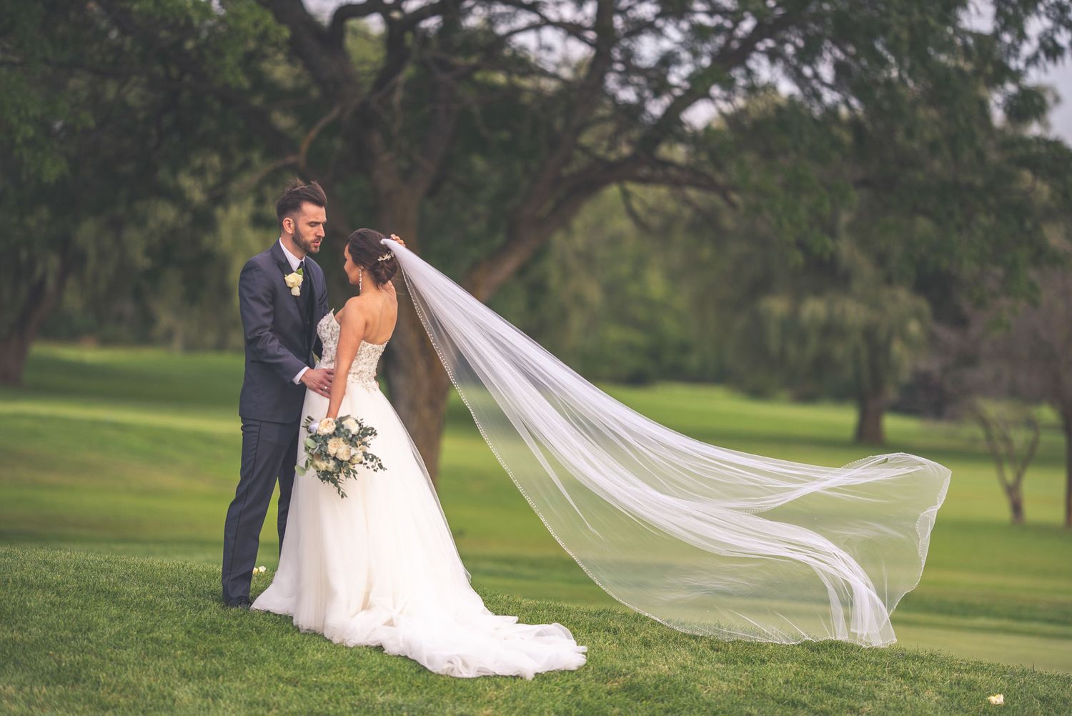 A romantic wedding photo series showing a couple in formal attire on a lush green golf course with a flowing veil.