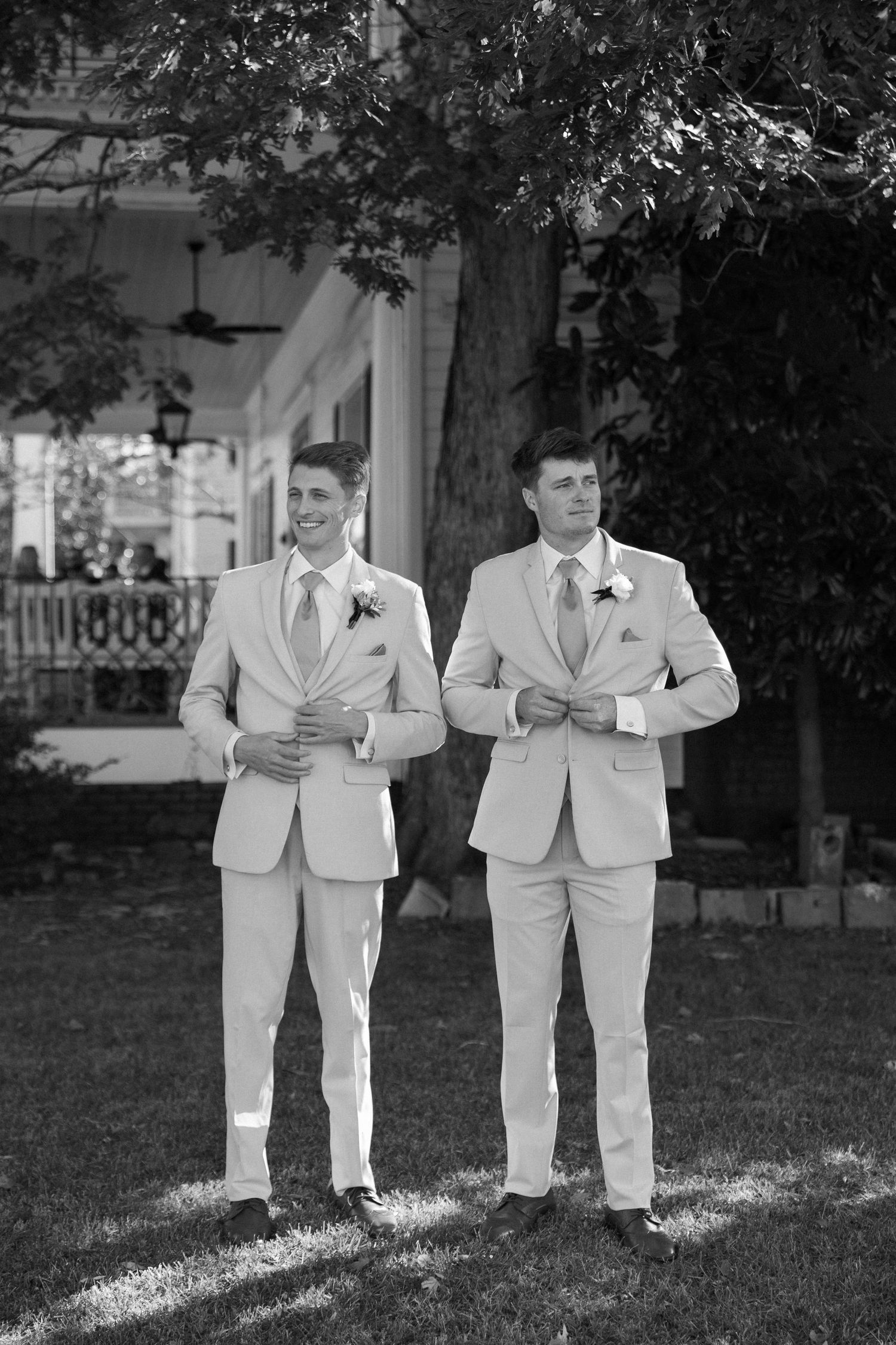 Two groomsmen in matching light colored suits stand together on a lawn in front of a white building at Lillian Gardens in Newnan, Georgia