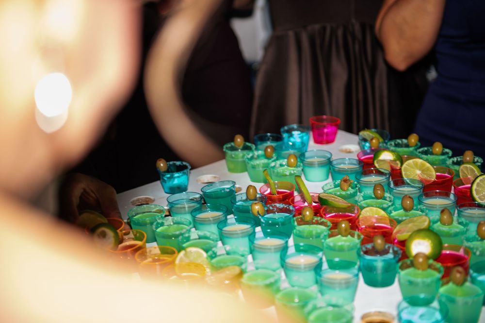 Colorful shot glasses lined up on a bar counter with vibrant red and green liquid drinks.
