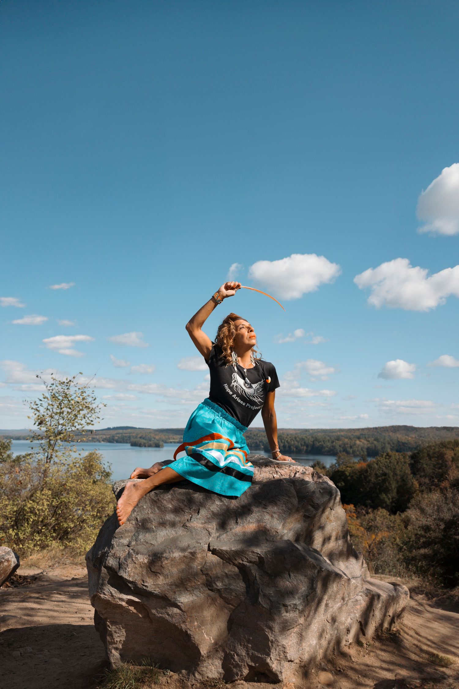 A sequence of yoga poses performed on a large rock formation overlooking a scenic mountain landscape on a sunny day.