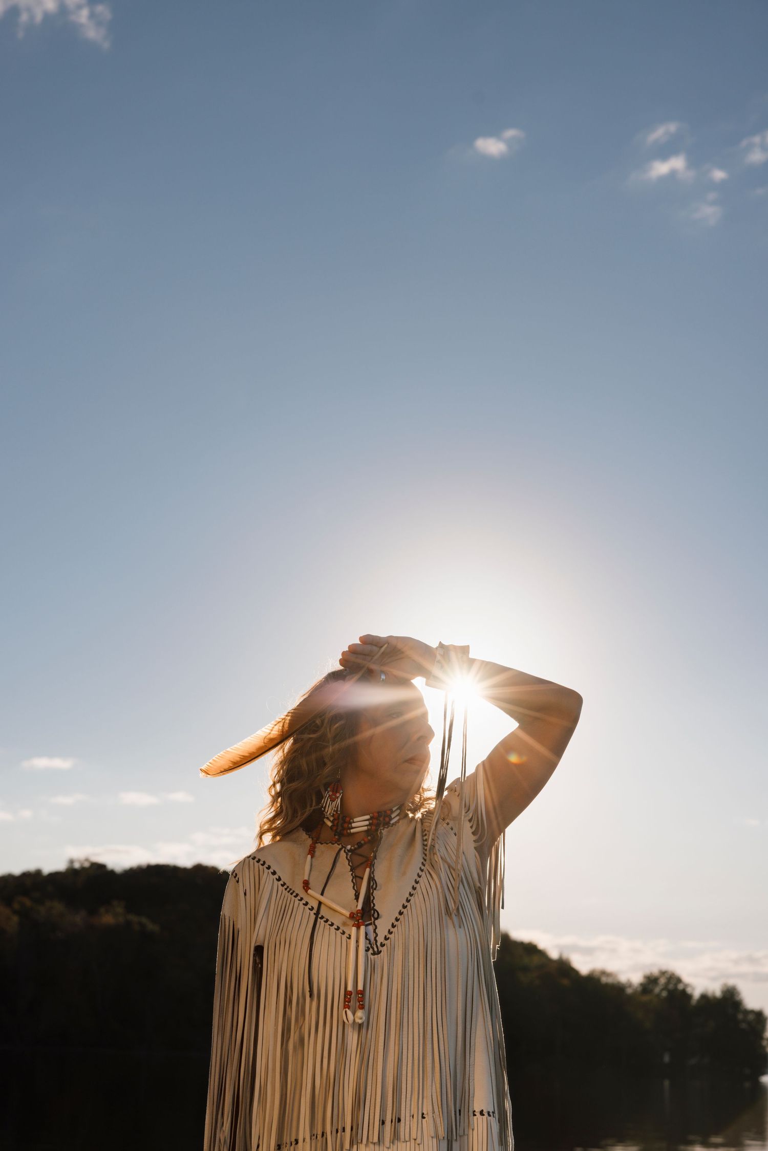 Sunlight streams through decorative fringe tassels of a bohemian style garment against a bright blue sky.