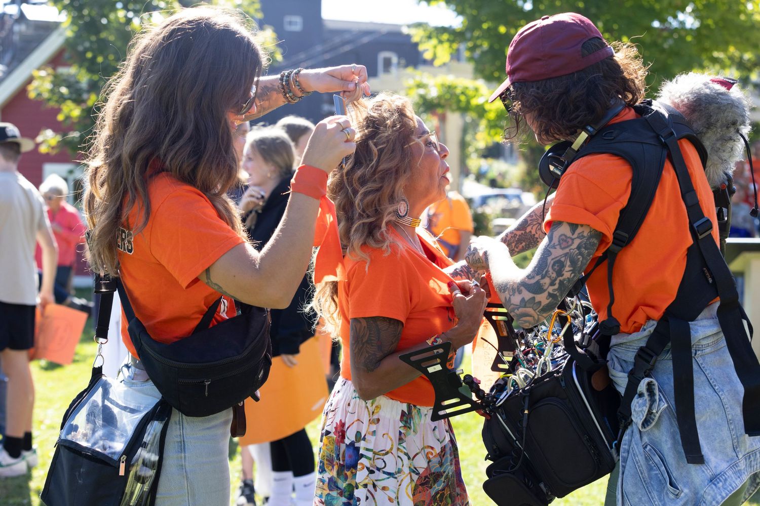 People in orange shirts and casual attire stand together outdoors during a sunny day event.