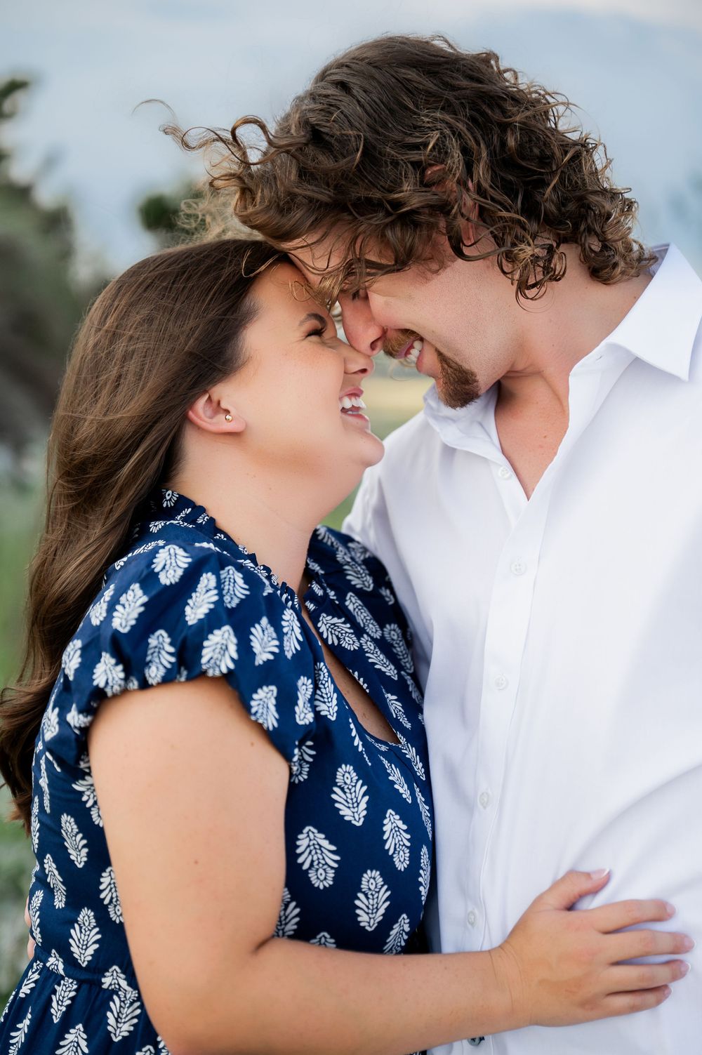 A romantic moment captured between a couple in blue and white attire against a coastal backdrop.